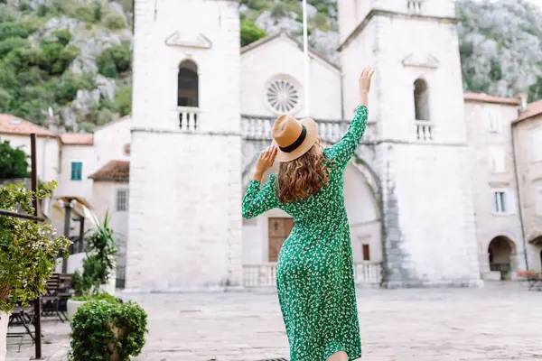 Parlak elbiseli ve şapkalı güzel bir turist eğleniyor ve şehir manzarasının tadını çıkarıyor. Genç bir kadın şehirde geziyor ve eğleniyor. Tatil, tatil, seyahat konsepti.