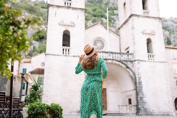 Parlak elbiseli ve şapkalı güzel bir turist eğleniyor ve şehir manzarasının tadını çıkarıyor. Genç bir kadın şehirde geziyor ve eğleniyor. Tatil, tatil, seyahat konsepti.