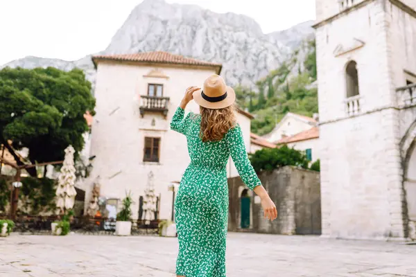 Parlak elbiseli ve şapkalı güzel bir turist eğleniyor ve şehir manzarasının tadını çıkarıyor. Genç bir kadın şehirde geziyor ve eğleniyor. Tatil, tatil, seyahat konsepti.