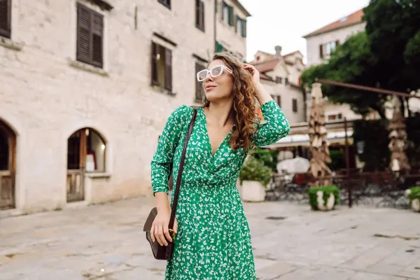 Parlak elbiseli ve şapkalı güzel bir turist eğleniyor ve şehir manzarasının tadını çıkarıyor. Genç bir kadın şehirde geziyor ve eğleniyor. Tatil, tatil, seyahat konsepti.