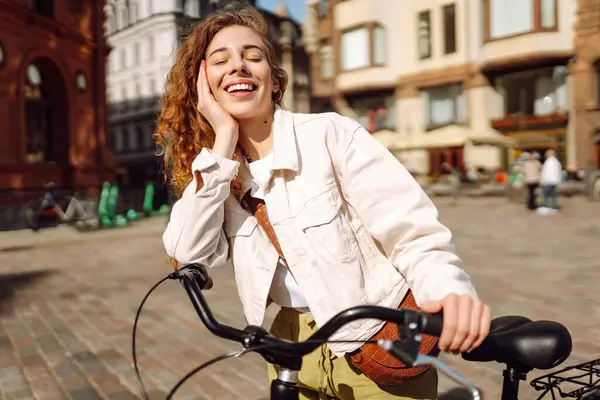 Gündelik giysiler içinde güzel bir kadın güneşli şehir sokaklarında bisiklet sürüyor. Yürüyüş, tatil, seyahat kavramı. Etkin yaşam biçimi.