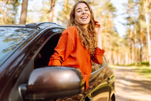 Kıvırcık saçlı genç bir kadının portresi arabanın camından gün batımını seyrediyor. Mutlu gezgin arabadan özgürlüğünü hissediyor. Özgürlük, macera konsepti.