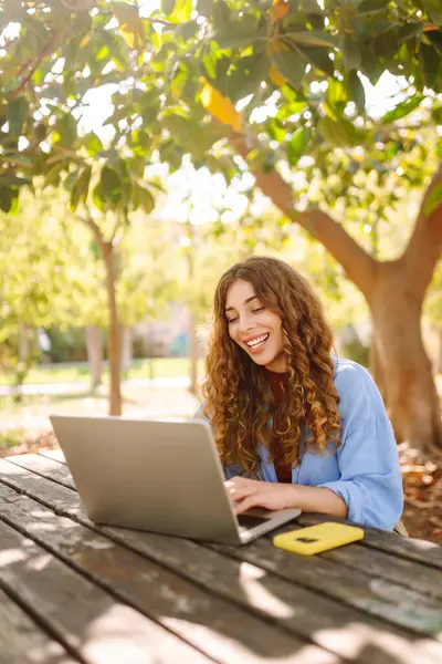 Parktaki bir masada dizüstü bilgisayarla çalışan genç bir kadın. Açık havada havanın tadını çıkaran mutlu kadın serbest yazar. Uzaktan çalışma konsepti. Yaşam biçimi.