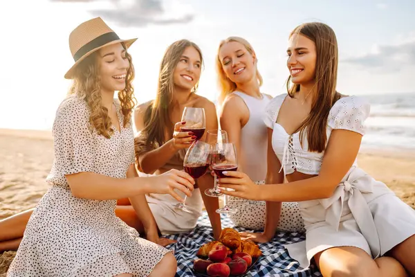 Mutlu kız arkadaşlar gün batımı kumsalında birlikte vakit geçiriyorlar. Ellerinde gözlüklerle dışarıda eğlenen dört güzel kadın. Arkadaşlık kavramı, eğlence. Yaşam biçimi.