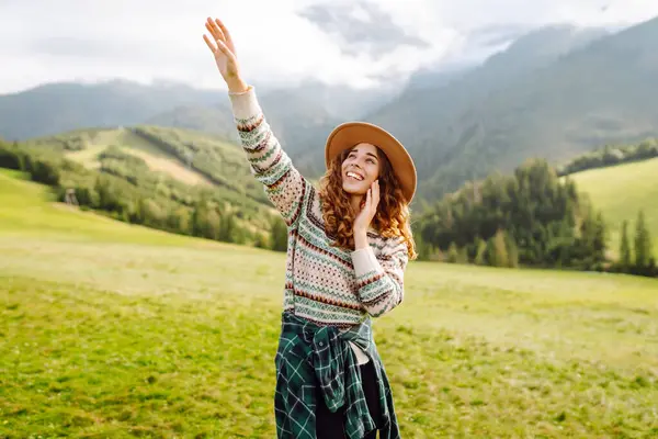 Yeşil tepelere karşı sevimli kadın gezgin özgürlüğü hissediyor. Şapkalı güzel kadın dağlarda güzel bir yerde eğleniyor. Yürüyüş, seyahat, özgürlük kavramı.