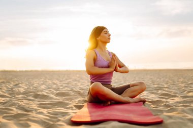 Spor kıyafetli genç bir kadın gün batımında yoga yapıyor. Atletik kadın doğada esneme hareketleri yapıyor. Dinlenme, rahatlama kavramı. Etkin yaşam biçimi.
