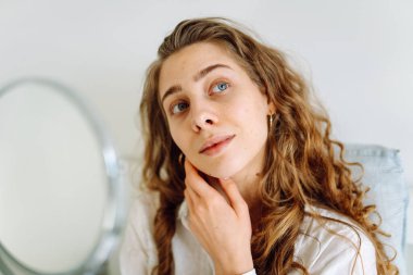 Genç bir kadının portresi küçük bir aynada yansımasına bakıyor, saçını düzeltiyor. Güzel bir kadın tenine dokunur, sivilcelerini inceler. Cilt bakımı, güzellik, doğallık kavramı.