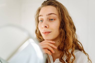 Genç bir kadının portresi küçük bir aynada yansımasına bakıyor, saçını düzeltiyor. Güzel bir kadın tenine dokunur, sivilcelerini inceler. Cilt bakımı, güzellik, doğallık kavramı.