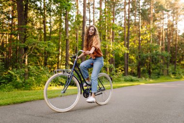 Genç bir kadın güneşli ormanda bisiklet sürmekten hoşlanıyor. Güzel bir turist gün batımında eğleniyor. Dinlenmek, yürümek. Etkin yaşam biçimi.