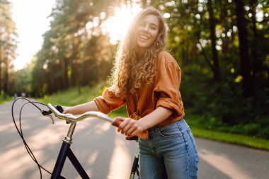 Genç bir kadın güneşli ormanda bisiklet sürmekten hoşlanıyor. Güzel bir turist gün batımında eğleniyor. Dinlenmek, yürümek. Etkin yaşam biçimi.
