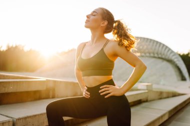 Spor yapan kadın gün batımında egzersiz yapıyor. Spor giyimli güzel bir kadın antrenmandan zevk alıyor ve dışarıda kendini güçlü hissediyor. Spor ve spor konsepti. Etkin yaşam biçimi.