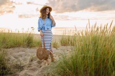 Hasır şapkalı gülümseyen kadın güneşli bir sahilde eğleniyor. Güzel bir kadın hafta sonunun tadını çıkarıyor ve dışarıda vakit geçiriyor. Tatil, keyif konsepti.