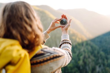 Uçurumun kenarında pusula tutan genç bayan gezginin arka görüntüsü. Sırt çantalı ve pusulası olan özgür hisseden ve dağ manzarasının tadını çıkaran bir kadın. Seyahat ve seyrüsefer kavramı.