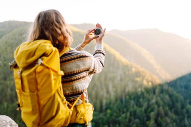 Uçurumun kenarında pusula tutan genç bayan gezginin arka görüntüsü. Sırt çantalı ve pusulası olan özgür hisseden ve dağ manzarasının tadını çıkaran bir kadın. Seyahat ve seyrüsefer kavramı.