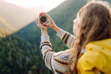 Uçurumun kenarında pusula tutan genç bayan gezginin arka görüntüsü. Sırt çantalı ve pusulası olan özgür hisseden ve dağ manzarasının tadını çıkaran bir kadın. Seyahat ve seyrüsefer kavramı.