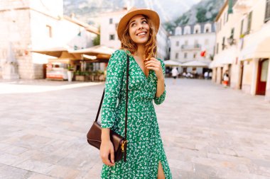 Parlak elbiseli ve şapkalı güzel bir kadın güneşli bir günde Avrupa 'nın eski sokaklarında yürüyor. Genç bir turist dışarıda güneşin doğuşunun tadını çıkarıyor. Turizm konsepti. Etkin yaşam biçimi.