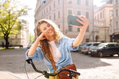 Güneşli şehir caddesinde bisikletiyle selfie çeken neşeli kadın portresi. Avrupa 'da yürüyen güzel bir kadın, blog yazıyor. Yürüme, blog konsepti. Etkin yaşam biçimi.