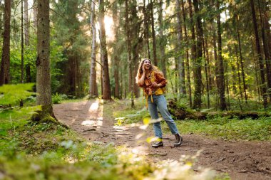 Sırt çantalı neşeli bayan gezgin gün batımında yürüyüş yapıyor. Kıvırcık saçlı güzel kadın ormanda özgürlüğü ve mutluluğu hissediyor. Macera konsepti.