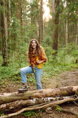 Sırt çantalı neşeli bayan gezgin gün batımında yürüyüş yapıyor. Kıvırcık saçlı güzel kadın ormanda özgürlüğü ve mutluluğu hissediyor. Macera konsepti.