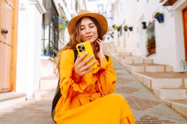 Şapkalı ve sırt çantalı güzel bir turist. Mesajlaşmalı ya da dışarıda elinde telefonla blog yazıyor. Telefonu olan, seyahatin ya da tatilin tadını çıkaran, sokaklarda yürüyen genç bir kadın. Etkin yaşam biçimi.