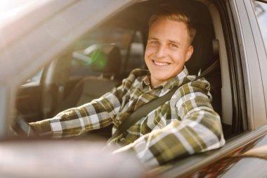 Kareli tişörtle araba süren genç bir adam güneşli havanın tadını çıkarıyor. Sürüş, ulaşım, seyahat kavramı.