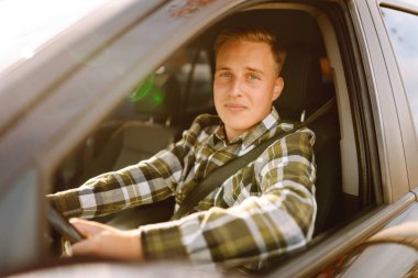 Kareli tişörtle araba süren genç bir adam güneşli havanın tadını çıkarıyor. Sürüş, ulaşım, seyahat kavramı.