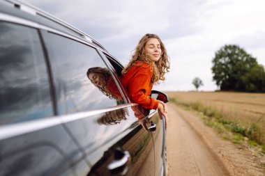 Mutlu kadın gezgin arabanın camından sarkan özgürlüğü hissediyor. Araba yolculuğundan hoşlanan genç bir kadın. Boş zaman kavramı, özgürlük. Seyahat tutkusu.