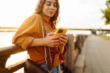 Telefonu olan güzel bir kadın gün batımı seti boyunca yürüyor. Genç bir turist havayı ve blogları sever. Boş zaman konsepti, blog. Etkin yaşam biçimi.