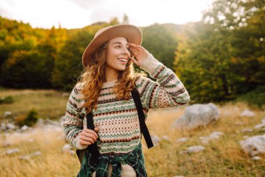 Şapkalı kadın gezgin kendini özgür hissediyor, dağlarda güneşli havanın tadını çıkarıyor. Seyahat tutkusu. Seyahat, tatil konsepti. Etkin yaşam biçimi.