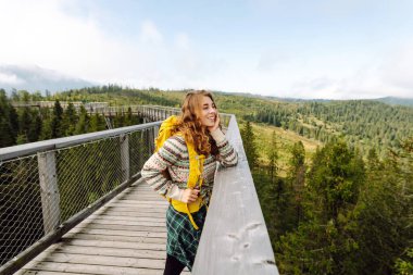 Sırt çantalı güzel bir bayan gezgin ahşap yürüyüş yolunda yürüyor. Genç bir kadın seyahat için özgürlük ve tutku hissediyor. Doğa, seyahat, tatil konsepti. Etkin yaşam biçimi.