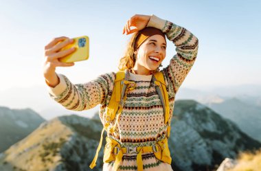 Yürüyüş ekipmanlarıyla dağda selfie çeken bir yürüyüşçü. Neşeli kadın özgürlüğü hissediyor ve gün batımının tadını çıkarıyor. Yürüyüş, macera konsepti. Etkin yaşam biçimi.