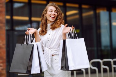 Alışveriş yaptıktan sonra çantalarını tutan modern giysili mutlu kadın portresi. Genç bir kadın dışarıda eğleniyor ve yeni alışverişlerden zevk alıyor. Tüketim kavramı, alışveriş.