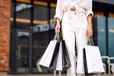 Alışveriş yaptıktan sonra çantalarını tutan modern giysili mutlu kadın portresi. Genç bir kadın dışarıda eğleniyor ve yeni alışverişlerden zevk alıyor. Tüketim kavramı, alışveriş.