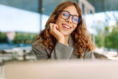 Gözlüklü ve dışarıda masada dizüstü bilgisayarı olan genç bir kadın. Gün batımında bir kafede dizüstü bilgisayarla çalışan güzel bir kadın. Serbest çalışma, eğlence, güzellik konsepti.