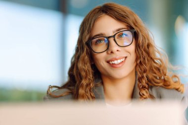 Gözlüklü ve dışarıda masada dizüstü bilgisayarı olan genç bir kadın. Gün batımında bir kafede dizüstü bilgisayarla çalışan güzel bir kadın. Serbest çalışma, eğlence, güzellik konsepti.
