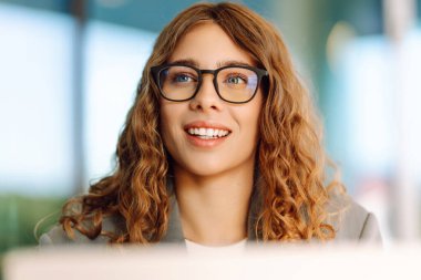 Gözlüklü ve dışarıda masada dizüstü bilgisayarı olan genç bir kadın. Gün batımında bir kafede dizüstü bilgisayarla çalışan güzel bir kadın. Serbest çalışma, eğlence, güzellik konsepti.