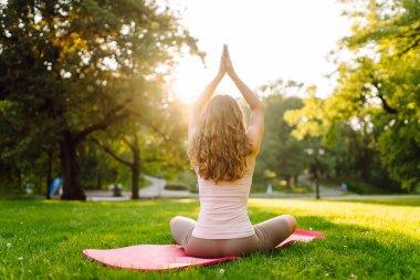 Sunny Park 'ta yoga minderi üzerinde egzersiz yapan genç bir kadın. Spor kıyafetli kadın dışarıda yoga yapıyor. Spor konsepti. Etkin yaşam biçimi.