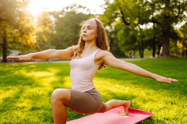 Sunny Park 'ta yoga minderi üzerinde egzersiz yapan genç bir kadın. Spor kıyafetli kadın dışarıda yoga yapıyor. Spor konsepti. Etkin yaşam biçimi.