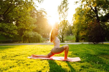 Sunny Park 'ta yoga minderi üzerinde egzersiz yapan genç bir kadın. Spor kıyafetli kadın dışarıda yoga yapıyor. Spor konsepti. Etkin yaşam biçimi.