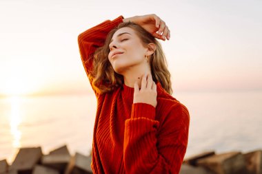 Güzel bir kadın gülümsüyor ve arka planda deniz manzarasıyla iskelede yürüyor. Günbatımının tadını çıkaran ve özgürlüğü hisseden genç bir kadın. Yürüyen konsept, özgürlük. Etkin yaşam biçimi.