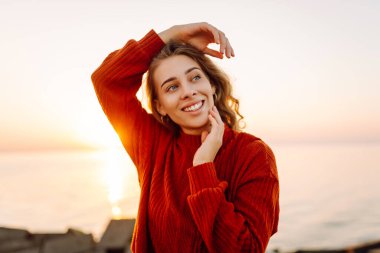 Güzel bir kadın gülümsüyor ve arka planda deniz manzarasıyla iskelede yürüyor. Günbatımının tadını çıkaran ve özgürlüğü hisseden genç bir kadın. Yürüyen konsept, özgürlük. Etkin yaşam biçimi.