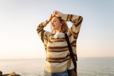 Gün batımında genç bir bayan yürüyüşçü kıyı şeridi boyunca yürüyor. Sırt çantalı güzel bir kadın havanın tadını çıkarıyor ve dışarıdaki özgürlüğün tadını çıkarıyor. Seyahat, keyif konsepti.