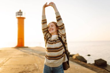 Gün batımında genç bir bayan yürüyüşçü kıyı şeridi boyunca yürüyor. Sırt çantalı güzel bir kadın havanın tadını çıkarıyor ve dışarıdaki özgürlüğün tadını çıkarıyor. Seyahat, keyif konsepti.
