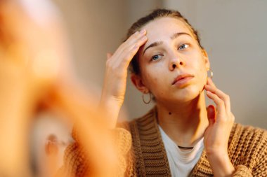 Yüzüne dokunan ve rahat bir odada aynaya bakan genç bir kadının portresi. Güzel bir kadın yüzündeki döküntüleri inceler, güzelliğinden zevk alır. Doğallık kavramı.