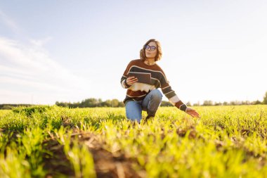 Dijital tabletli genç kadın çiftçi, tarım alanındaki genç bitkileri inceliyor. Kadın tarım uzmanı elinde bir tablet tutuyor ve filizlerin kalitesini kontrol ediyor. Bahçe konsepti.