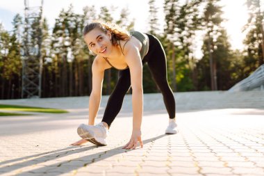 Sportif kadın dışarıda egzersiz yapıyor. Spor giyim sektöründe gün batımında parkta egzersiz yapan güzel bir kadın. Spor konsepti, rutin. Etkin yaşam biçimi.