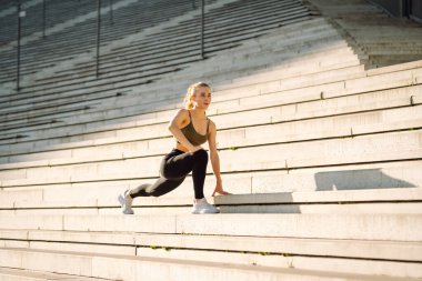 Sportif kadın dışarıda egzersiz yapıyor. Spor giyim sektöründe gün batımında parkta egzersiz yapan güzel bir kadın. Spor konsepti, rutin. Etkin yaşam biçimi.