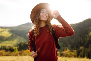 Parlak yeşil vadiyi gezen sırt çantalı güzel bir turist. Şapkalı genç bir kadın günbatımının ve doğanın tadını çıkarıyor. Seyahat, doğa ve özgürlük kavramı. Etkin yaşam biçimi.