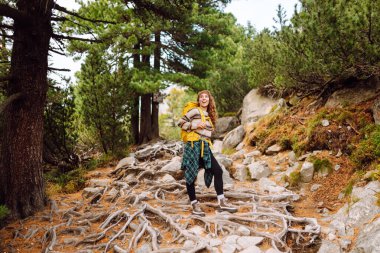 Sırt çantalı genç bayan yürüyüşçü yemyeşil ormanda kayalık yolda yürüyor. Güneşli bir günde doğa ile eğlenen mutlu kadın yürüyüşçü. Macera, eğlence konsepti. Etkin yaşam biçimi.