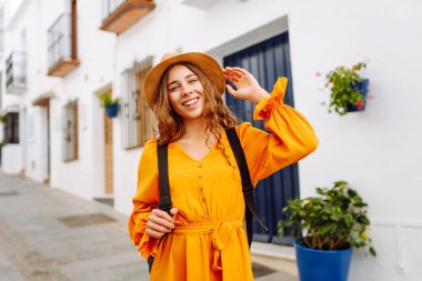 Dağlarda küçük bir kasabada gezen şapkalı ve parlak elbiseli bir kadın turist. Yürüyüşten, havadan ve mimariden hoşlanan güzel bir kadın. Seyahat, yürüyüş konsepti.